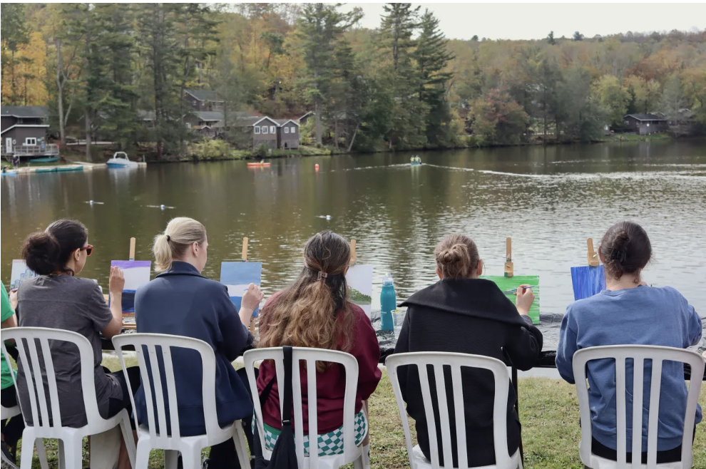 A group of woman sitting and painting at the lake 